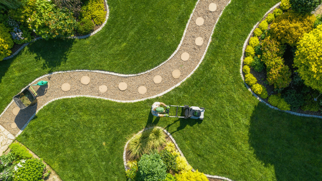 Ariel Shot of Person mowing lawn along manicured stone path