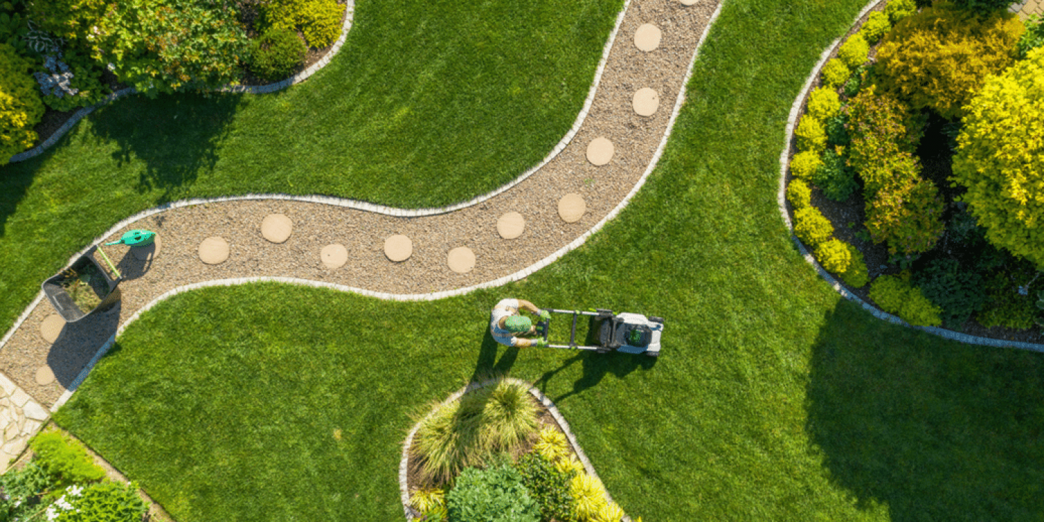 Ariel Shot of Person mowing lawn along manicured stone path